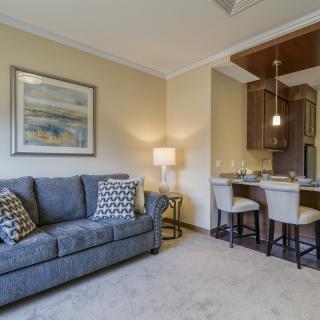 A cozy living room with a sofa and artwork, adjacent to a modern kitchen area with bar stools.