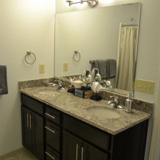 A neatly arranged bathroom with a large mirror, marble countertop, and stylish vanity.