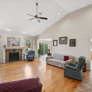 Spacious living room with hardwood flooring, featuring a sofa, armchairs, and a fireplace under a ceiling fan.