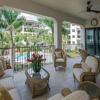 A cozy balcony with wicker furniture overlooks a lush tropical pool area.