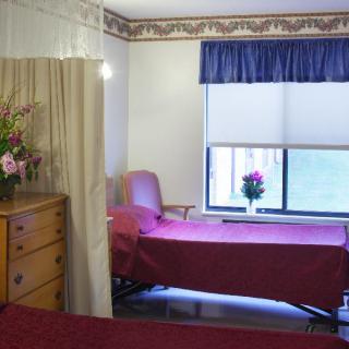 A simple hospital room with a single bed, a window adorned with flowers, and a dresser.