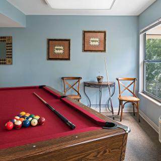 A cozy game room featuring a red-felt pool table beside a window and seating area.