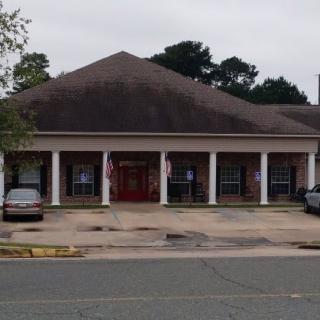A small commercial building with a parking area in front, set against an overcast sky.
