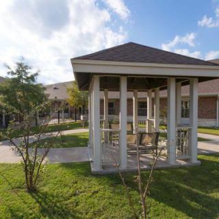 An outdoor gazebo on a grassy lawn near a building under a clear blue sky.