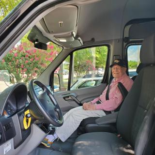 A person sits in the driver's seat of a parked van, wearing a seatbelt.