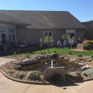 A group of people sit outside near a garden pond on a sunny day.