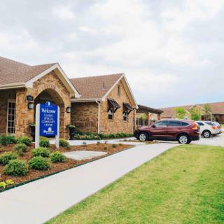 A healthcare facility featuring brick architecture, well-maintained landscaping, and a spacious parking lot under a cloudy sky.