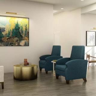 A modern living room with blue chairs, a gold coffee table, and landscape artwork on the wall.