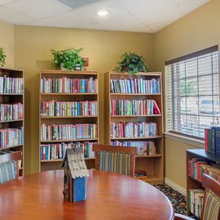 A cozy library room with bookshelves filled with books, a round table, and chairs.