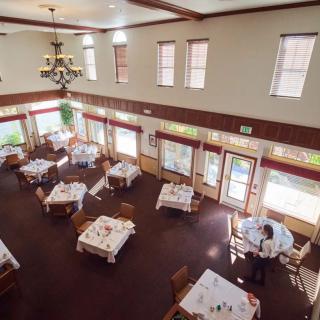 An empty restaurant dining room with neatly arranged tables and chairs, illuminated by natural light from the windows.
