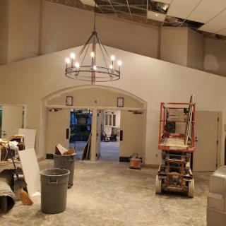A view of an interior space undergoing renovation, featuring a chandelier and construction materials.