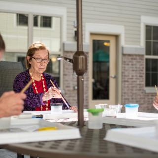 A group of elderly individuals engaged in painting crafts outdoors.