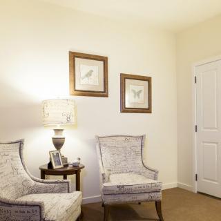 A cozy corner featuring two upholstered chairs, a small side table with a lamp, and framed artwork on the wall.