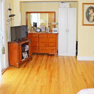 A cozy bedroom with hardwood floors, featuring a dresser with a mirror, a TV stand, and a closet.