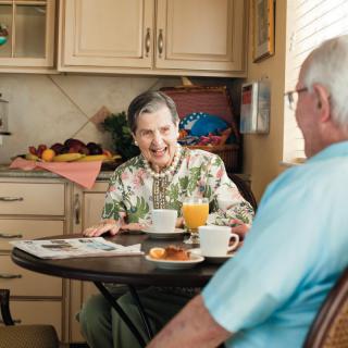 An elderly couple enjoying breakfast together at their kitchen table.