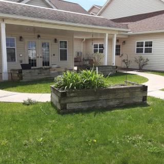A house with a patio and garden area featuring a wooden planter filled with greenery.