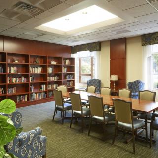 A well-lit library conference room with bookshelves, a large table, and chairs for meetings.