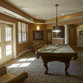 A cozy gaming room featuring a pool table, comfortable seating, and warm brown tones.