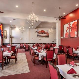 A stylish restaurant interior featuring red chairs and white tablecloths, illuminated by elegant chandeliers.