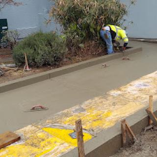 A worker is pouring and smoothing concrete in a landscaping area.