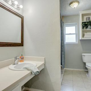 A clean and bright bathroom featuring a sink, mirror, toilet, and window with storage shelves.