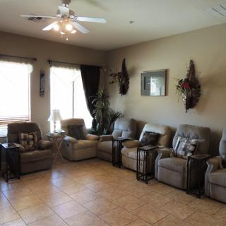 A cozy living room with multiple recliners arranged in a row, tiled flooring, and natural light streaming through the windows.