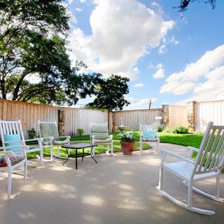 A sunny patio with white rocking chairs and a small garden area.