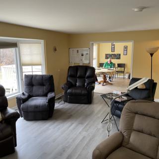 A cozy living room featuring multiple recliner chairs and a large window, with a view into the adjoining room.
