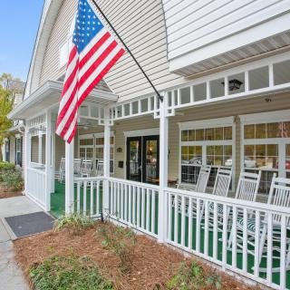 A charming house with a porch featuring rocking chairs and an American flag.