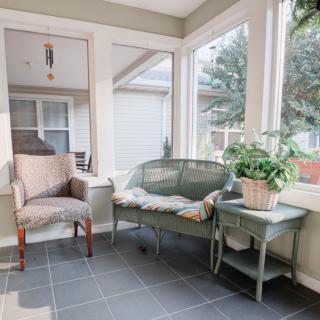 A cozy sunroom featuring a cushioned bench, an upholstered chair, and a side table with a potted plant.