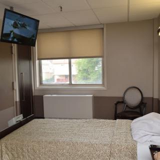 A view of a hospital room featuring an unmade bed, a television, and a window.