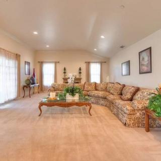 A spacious living room with a large patterned sofa, glass coffee table, decorative plants, and wall art.