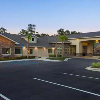 A modern building with a large parking lot and surrounding landscape at dusk.