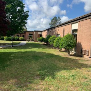 A serene view of a brick building surrounded by lush greenery and a clear blue sky.