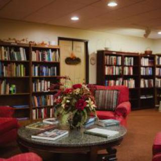 A cozy reading room with red armchairs, a round table with flowers, and bookshelves filled with books.