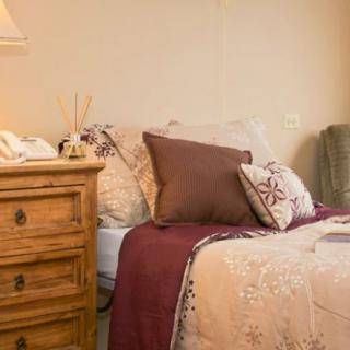 A cozy bedroom with a neatly made bed, decorative pillows, and a wooden nightstand with a lamp.