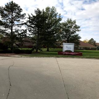 A view of a building with a sign surrounded by trees and a paved area.