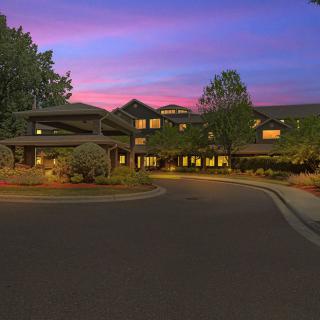A scenic view of a building at sunset with a driveway and surrounding trees.