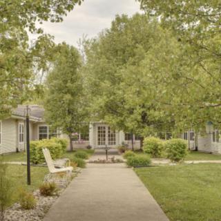A serene garden pathway surrounded by lush greenery and quaint buildings.