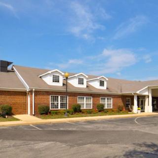 A brick building with a light-colored roof and multiple windows under a clear blue sky.