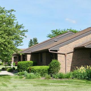 A row of well-kept single-story brick houses surrounded by lush greenery and manicured lawns.