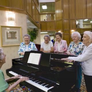 A group of elderly individuals gathered around a piano, enjoying a musical moment together indoors.