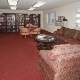 A cozy library room with shelves full of books, comfortable seating, and a carpeted floor.