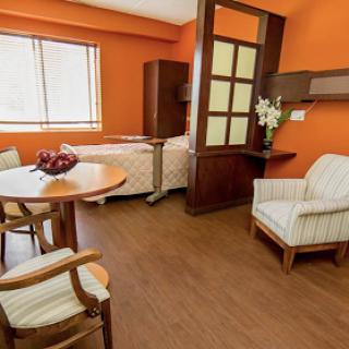 A peaceful and inviting hospital room featuring warm orange walls, a comfortable bed, and seating area with modern furnishings.
