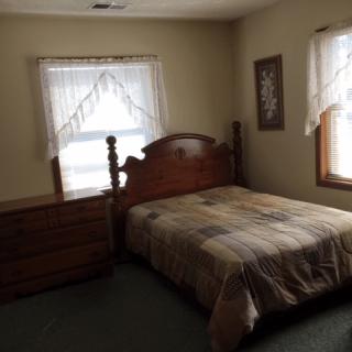 A cozy bedroom with a wooden bed, dresser, and windows adorned with lace curtains.