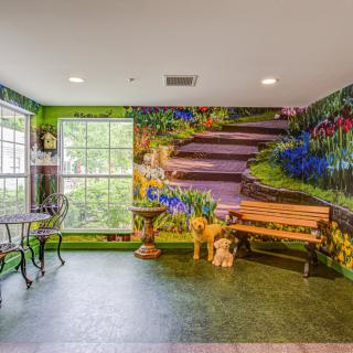 A room with a nature-themed mural featuring a staircase, vibrant flowers, and greenery, along with a small table and chairs by the window.
