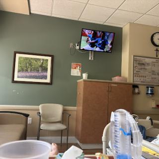A view of a hospital waiting room with a TV displaying content, comfortable seating, and medical supplies.