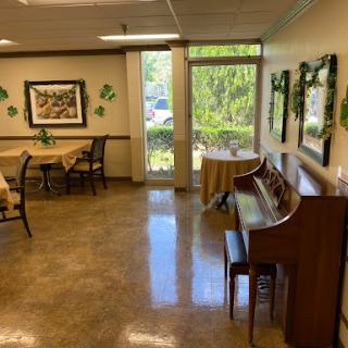A cozy lobby area featuring a piano, tables, and ample natural light from large windows.