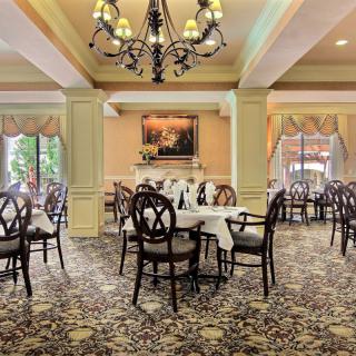 An elegant dining room with neatly arranged tables and chairs, featuring a beautiful chandelier and carpeted flooring.