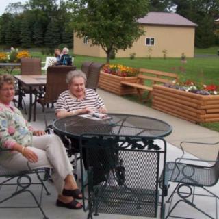 Two people sitting and relaxing at an outdoor patio table in a garden setting.